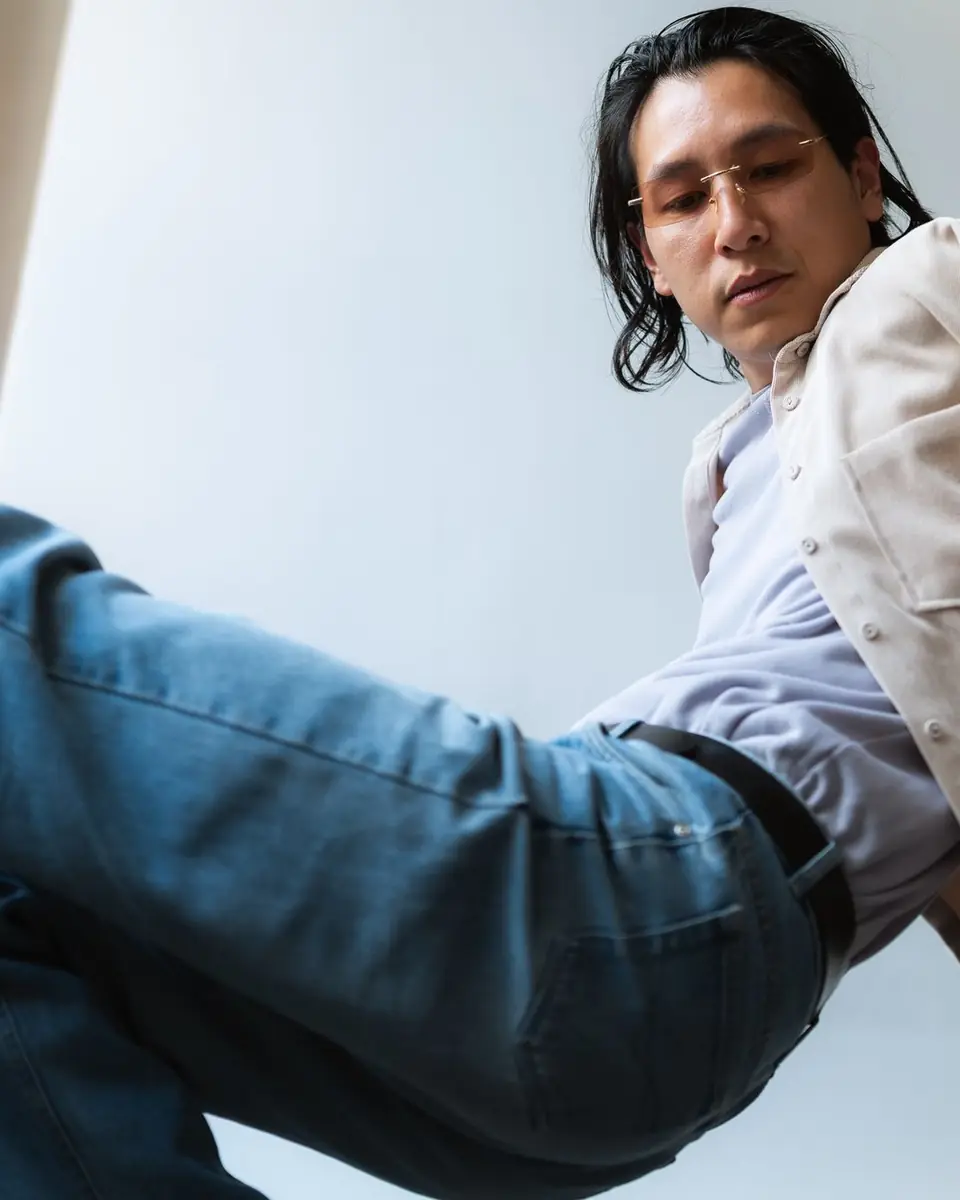 Homme assis en chemise claire et jeans, dans une pose décontractée