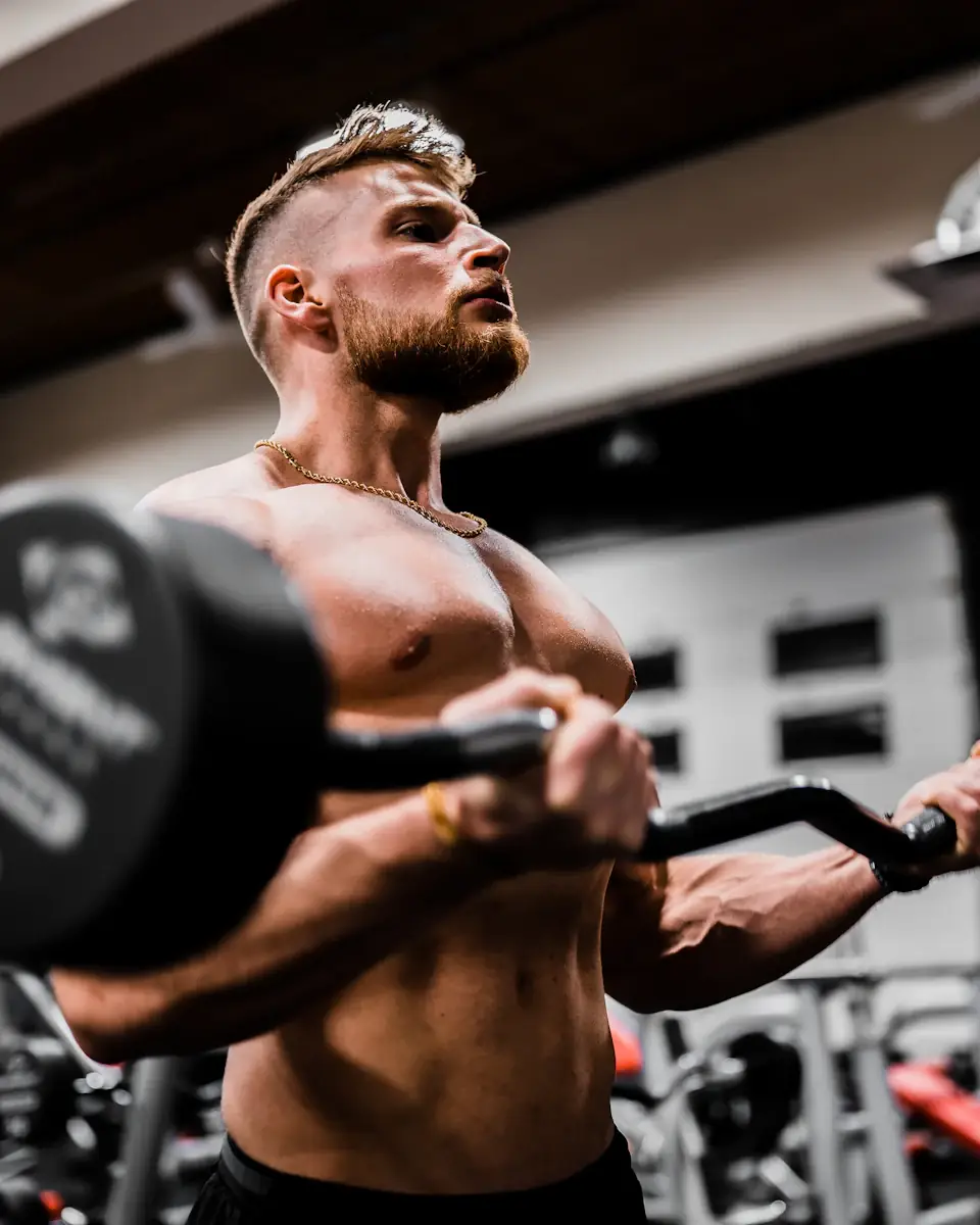 Athlète torse nu soulevant une barre, musculature éclairée dans une salle de sport